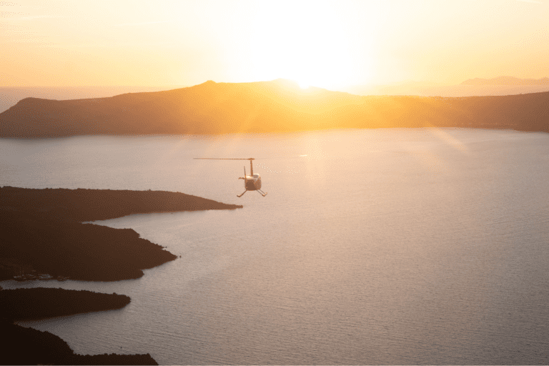 A helicopter flies over the Aegean Sea at sunset near Santorini, Greece.
