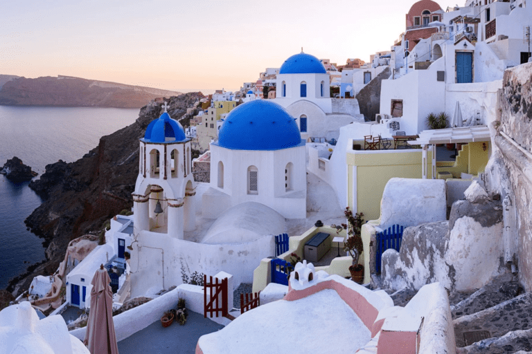 Panoramic view of Santorini's iconic whitewashed buildings and blue-domed churches at sunset, overlooking the Aegean Sea