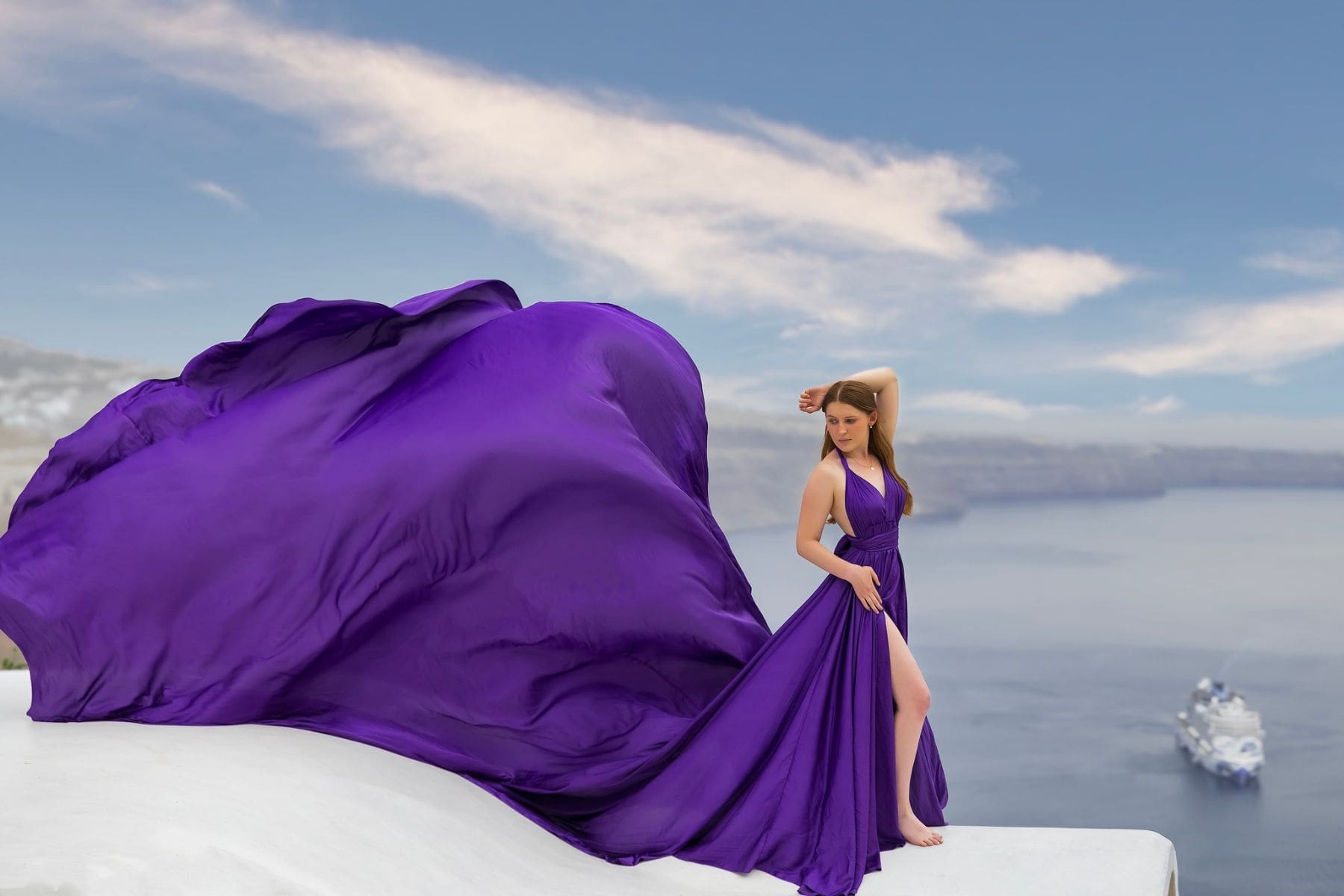 A woman in a flowing Santorini flying dress poses against the stunning backdrop of the caldera.
