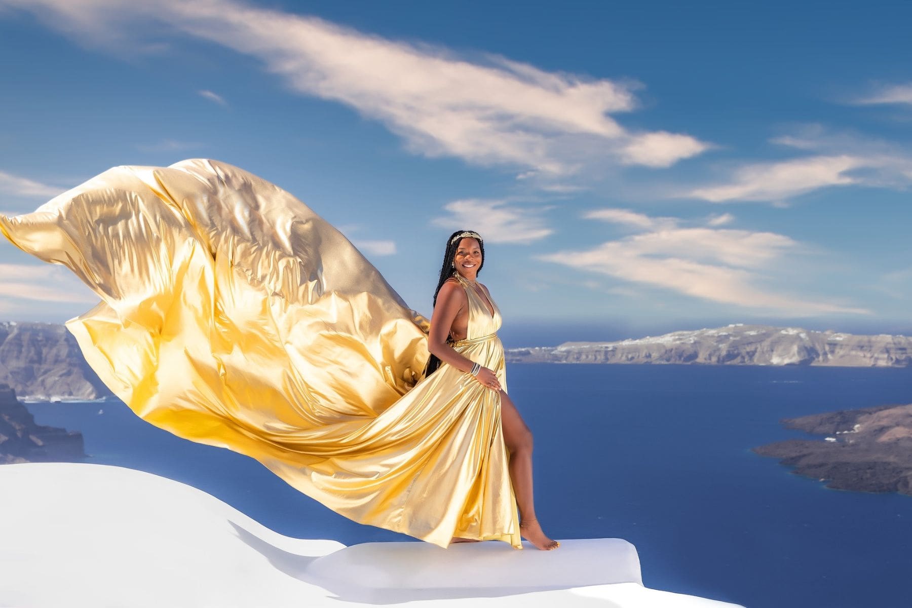 A woman in a flowing Santorini flying dress poses against the stunning backdrop of the caldera.