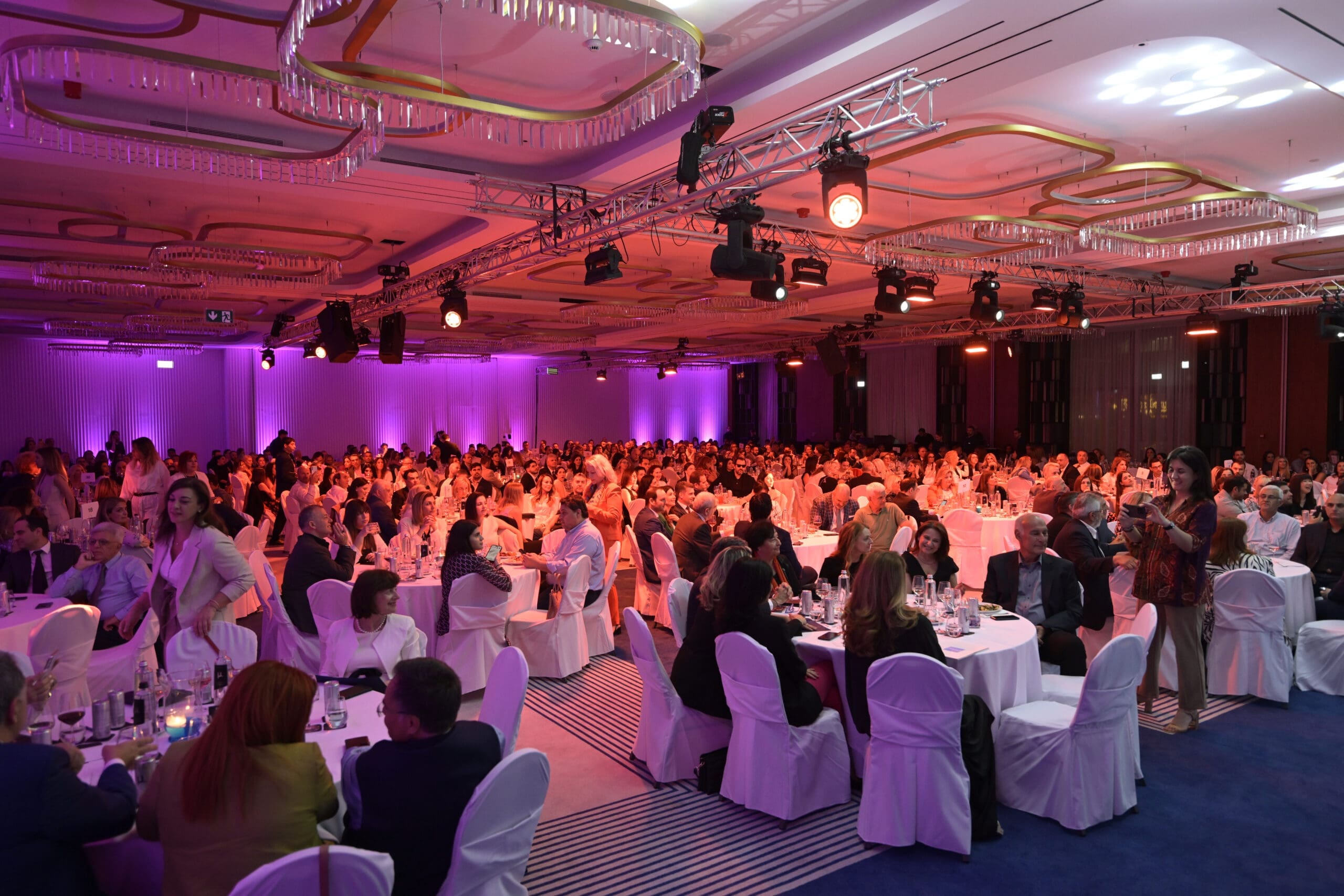 A large ballroom filled with people at tables, lit with pink and red lighting for an awards ceremony.