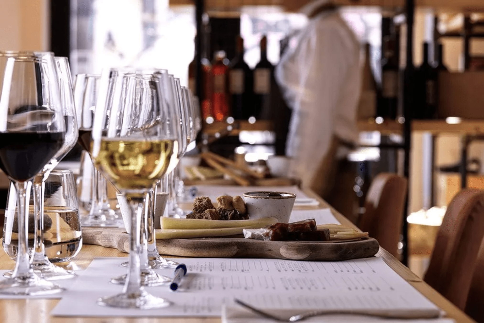 Wine glasses filled with red and white wine, along with a wooden board of cheese and snacks, are arranged on tasting sheets at an Athens wine tasting.