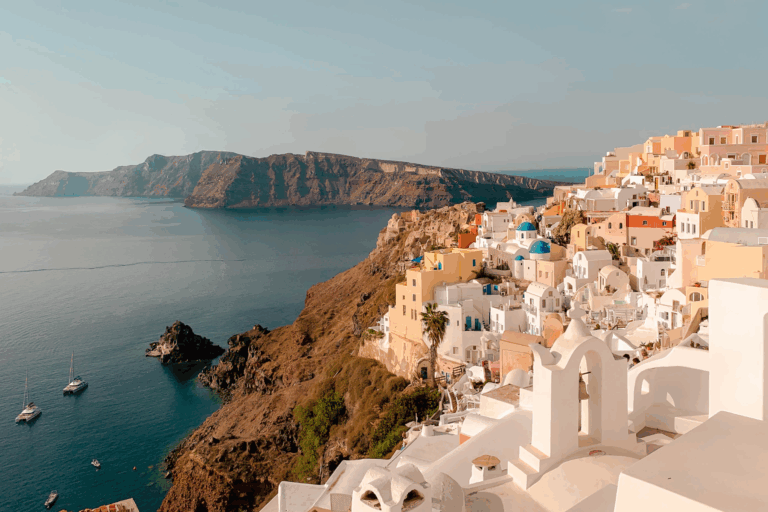 A scenic view of Oia, Santorini, showcasing white buildings with blue domes cascading down the cliffside toward the Aegean Sea.