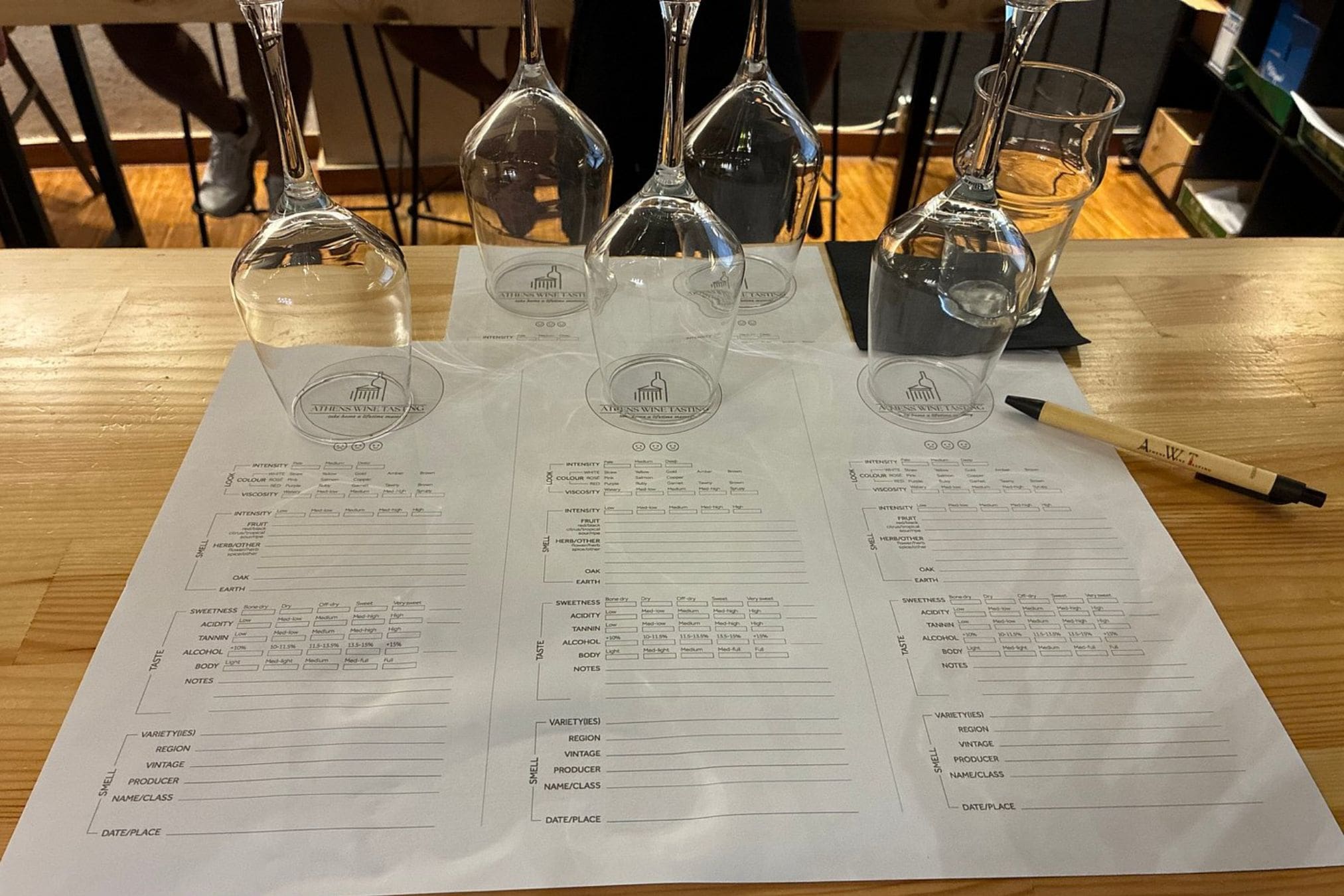 Wine glasses and tasting sheets on a wooden table during an Athens Wine Tasting workshop.