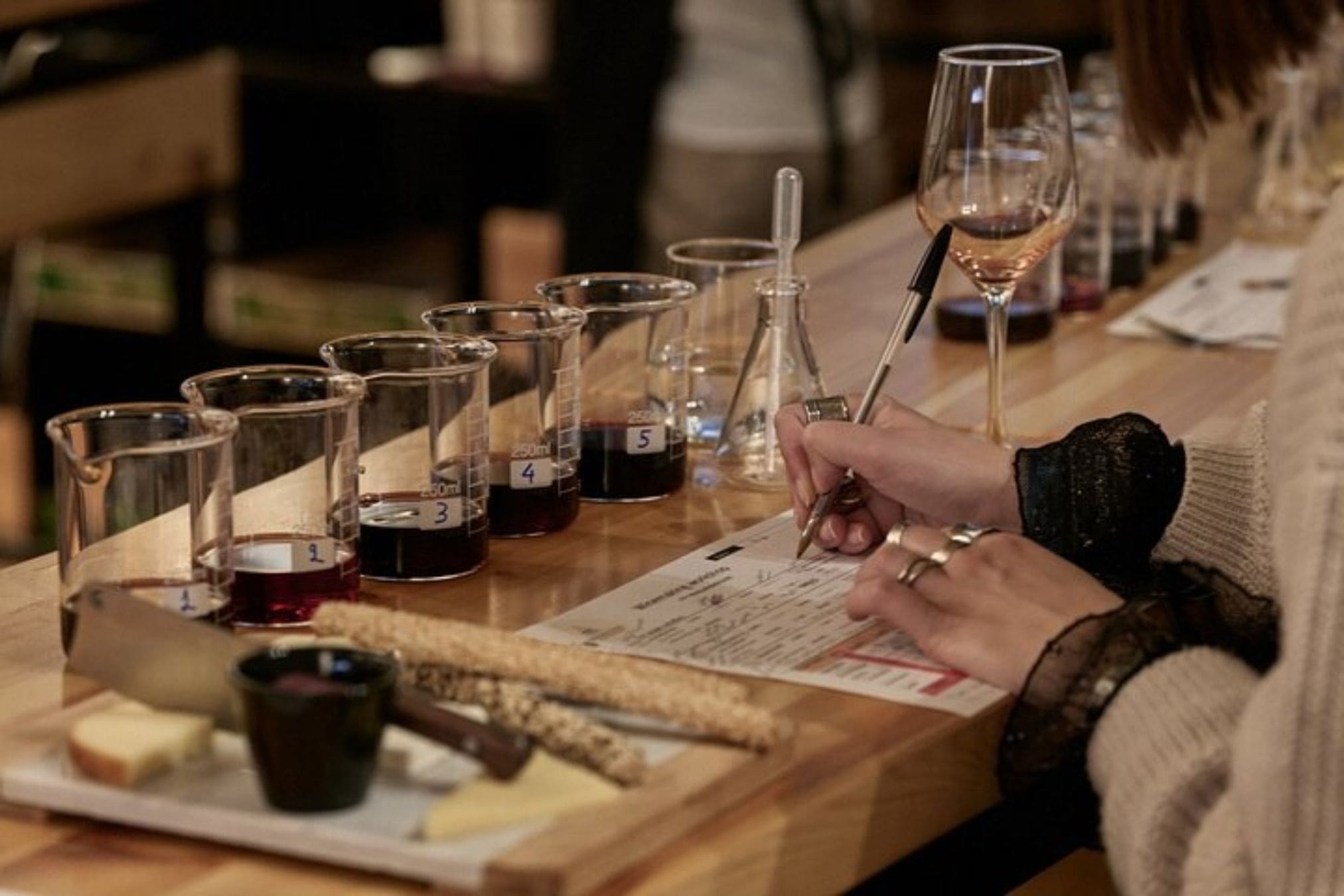 A person is tasting and making notes on different wines during a winemaking workshop. Title: Wine Tasting Notes
