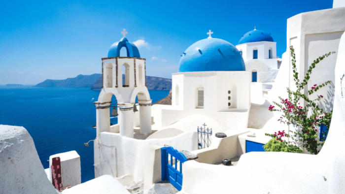 santorini blue domes, whitewashed church complex with blue domes, bell tower, and bright blue door overlooking the sea