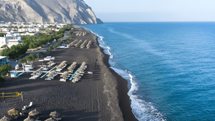 Black sand beach in Santorini with sunbeds and umbrellas along the coastline, one of the top beach activities to do in Santorini during vacation.