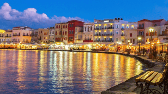 Chania Old Town waterfront in Crete at dusk with colorful buildings and lights reflecting on the harbor.